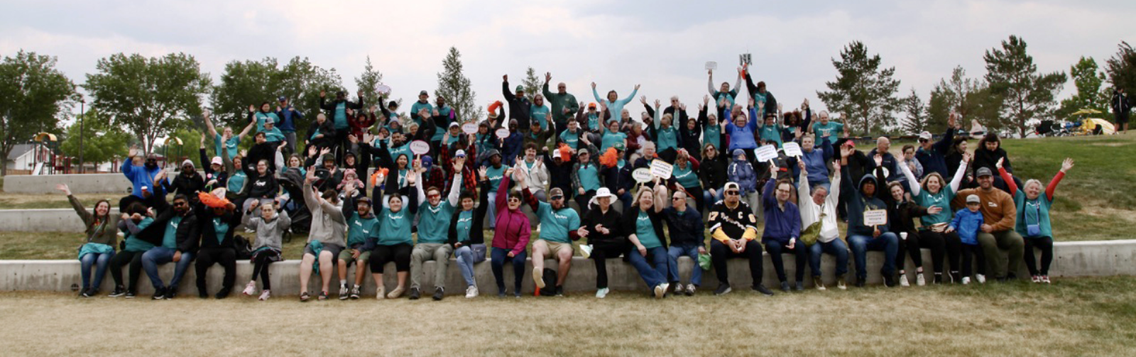 A large group of people sitting and standing on outdoor steps, cheering with raised arms, holding signs, under a cloudy sky.