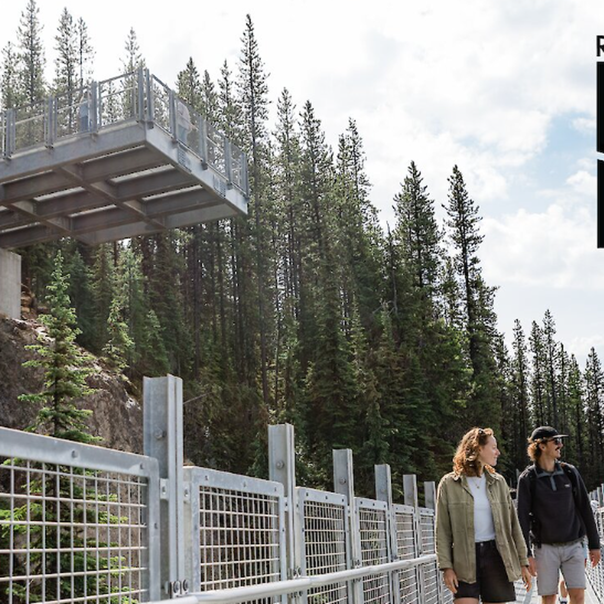 Two people walk on a metal walkway surrounded by pine trees, with a viewing platform above. Text reads "Revelstoke High Line."