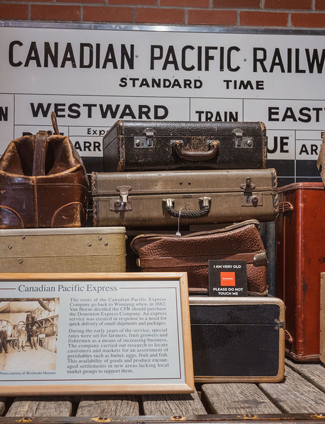 A stack of vintage suitcases and crates in front of a Canadian Pacific Railway sign, with a framed information board about Canadian Pacific Express.