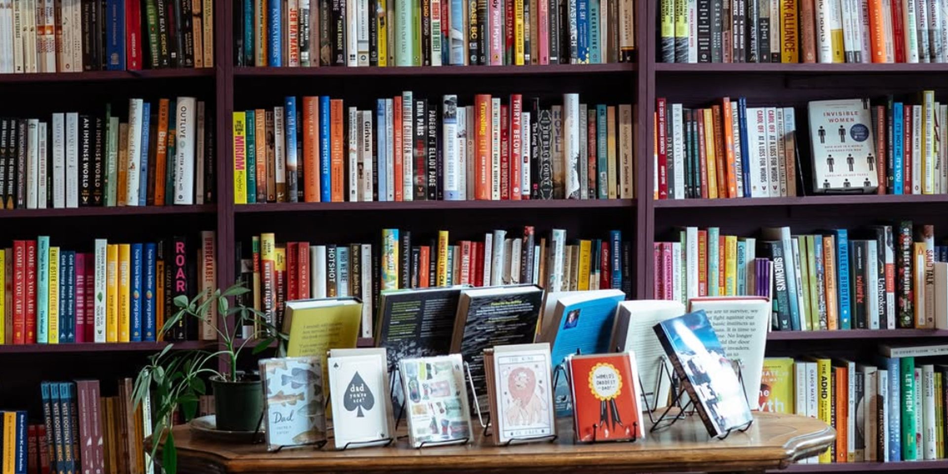 A cozy bookstore corner with shelves full of nonfiction books, a wooden table displaying featured titles, and a red patterned rug.