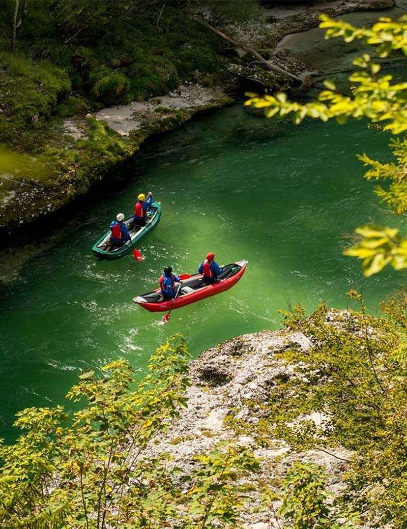 People kayaking on a vibrant green river, surrounded by lush greenery and rocky banks.
