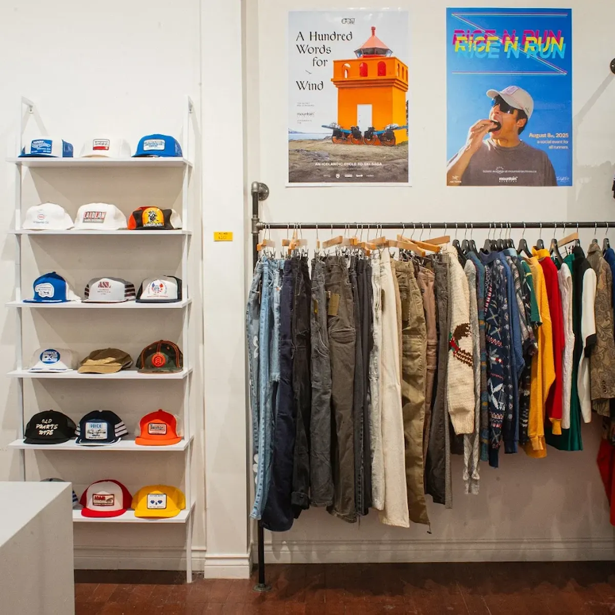 Clothing store interior with hats on shelves, various pants and shirts on racks, and colorful posters on the wall.
