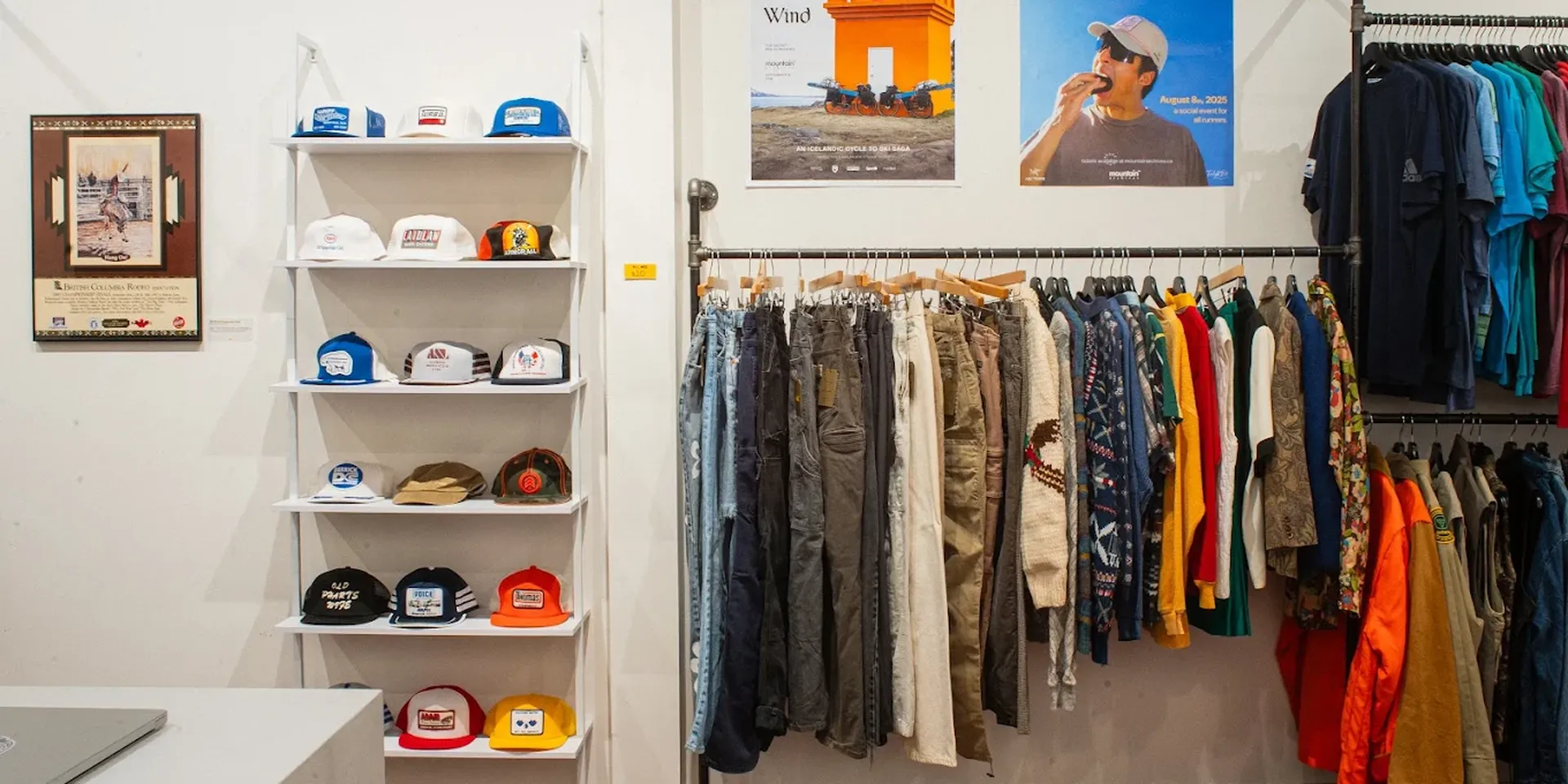 Clothing store interior with hats on shelves, various pants and shirts on racks, and colorful posters on the wall.
