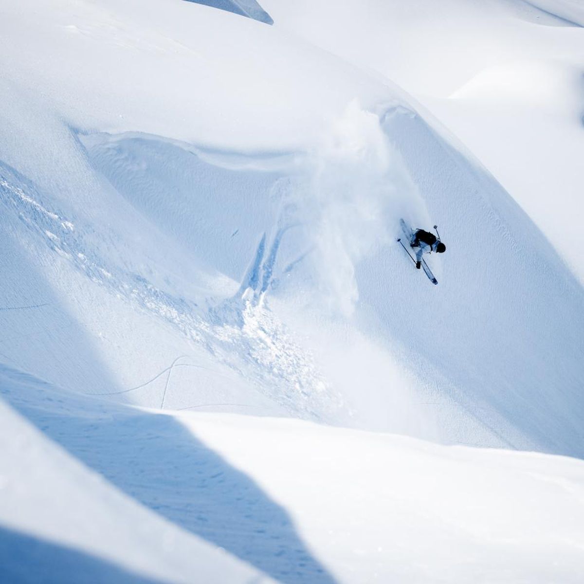 A skier performs a jump on a snowy slope, leaving a trail of powder in a pristine, mountainous landscape.