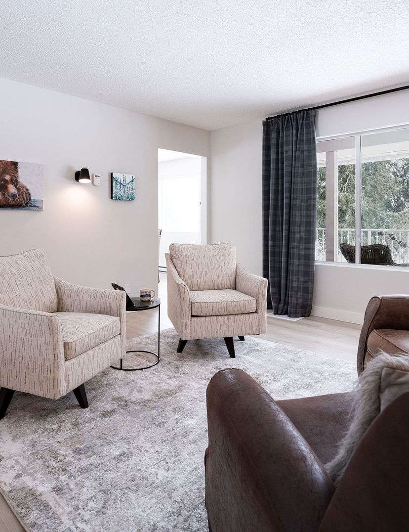 Cozy living room with two armchairs, two brown chairs, a rug, animal paintings, and a large window with drapes overlooking a snowy landscape.