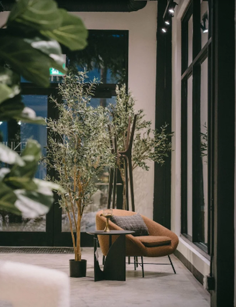 Modern interior with a brown chair, small table, and potted plants near large windows, creating a cozy and stylish atmosphere.