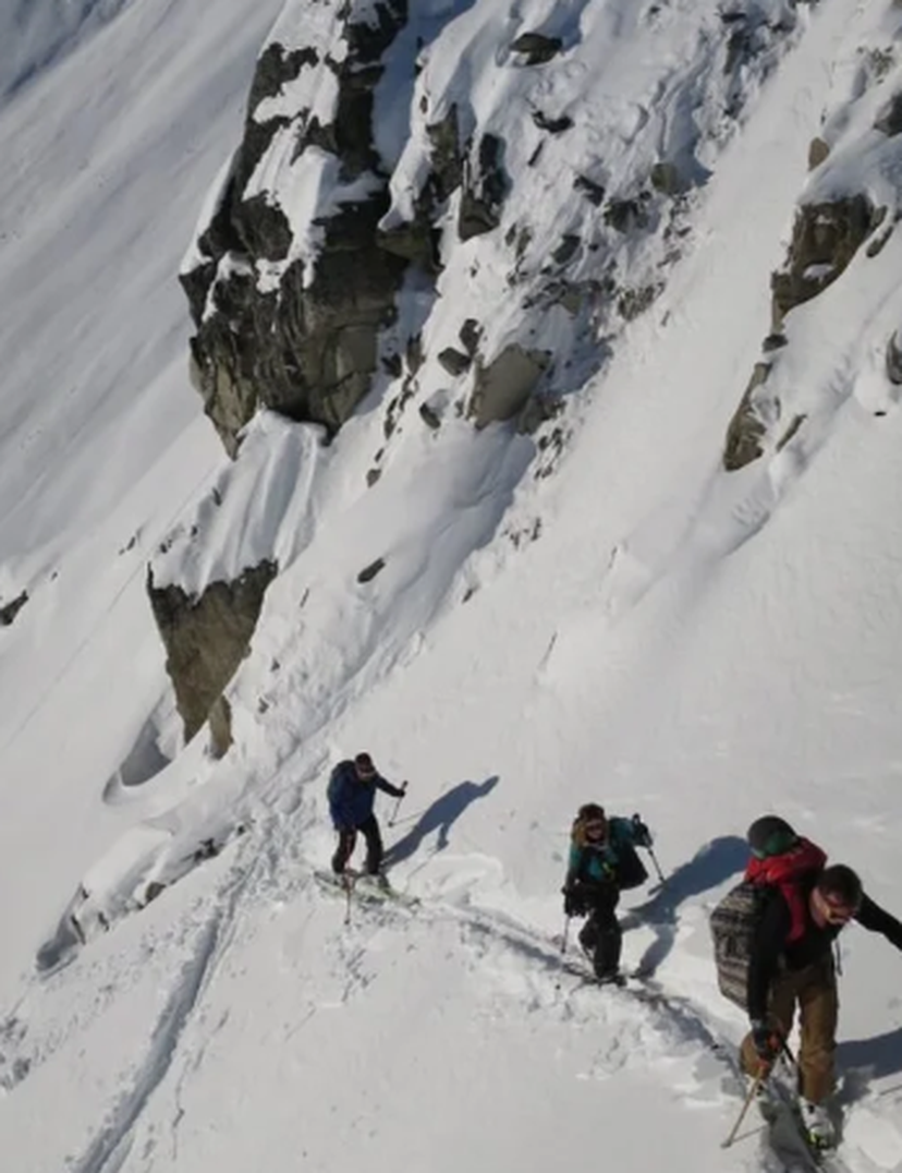 three backcountry skiers walking up steep pitch in mountain terrain