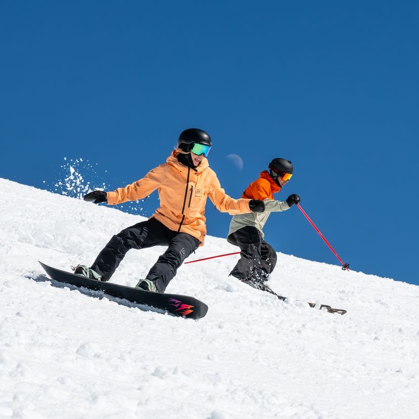 skier and snowboarder skiing with half moon in background