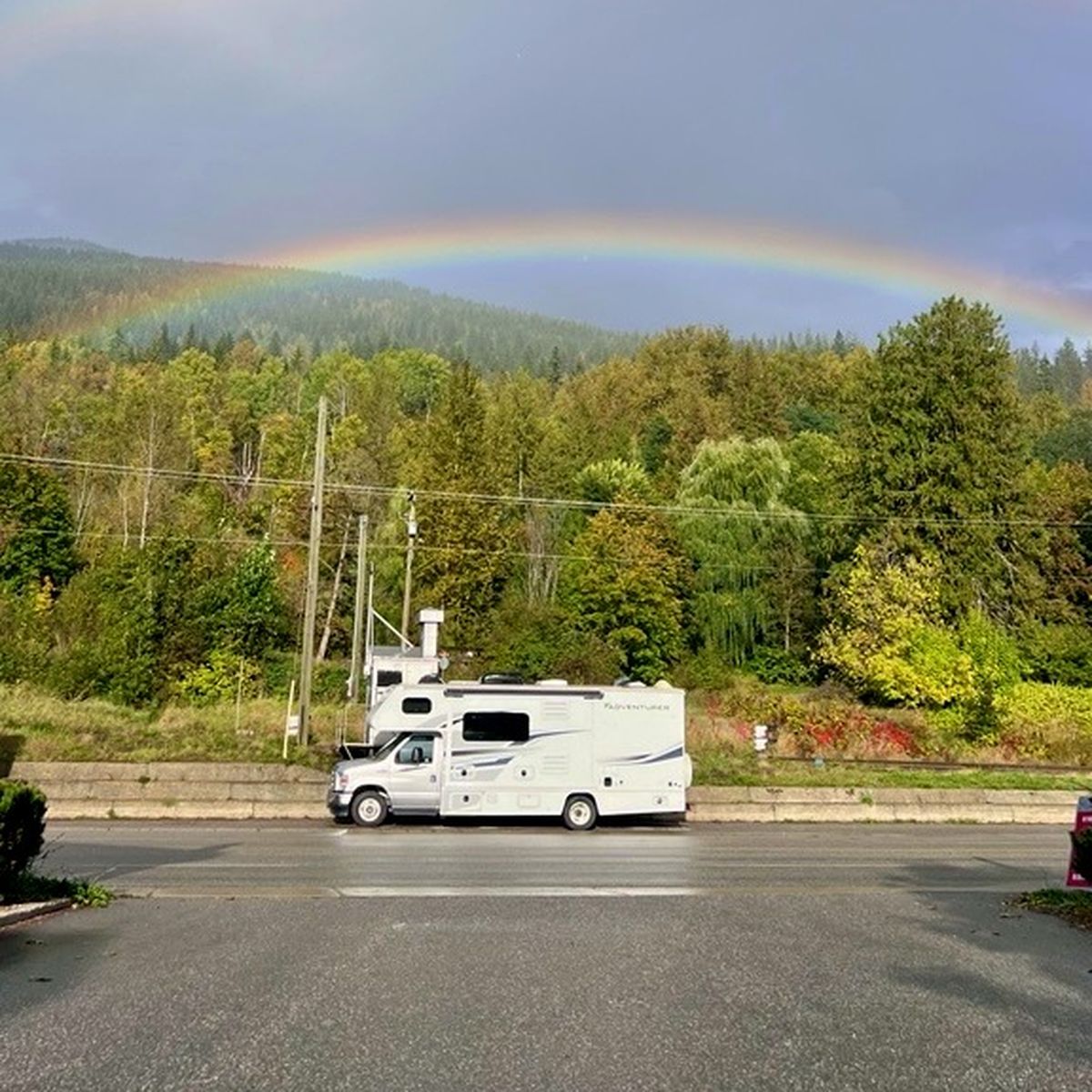 rv parked on side of the road underneath a rainbow