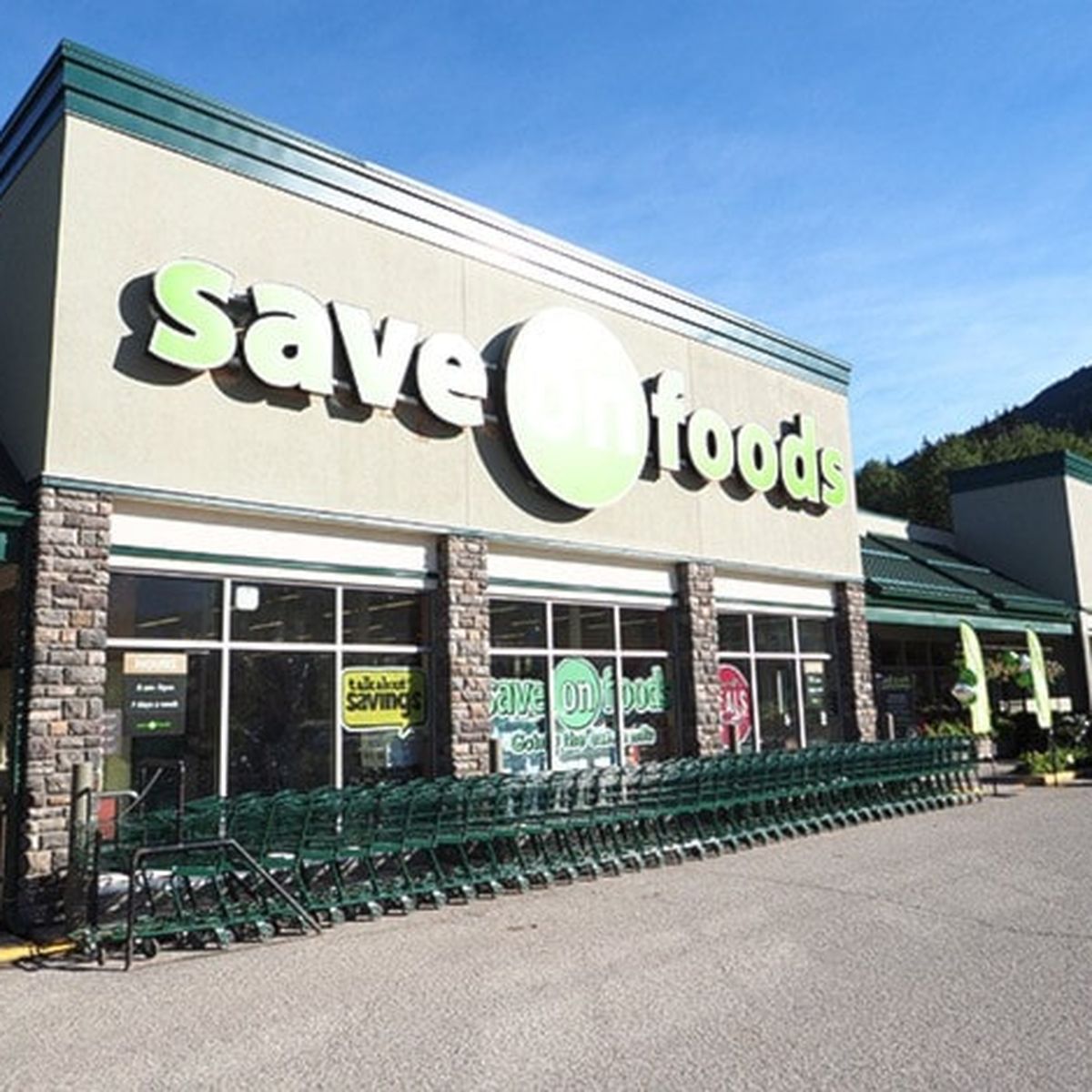 Exterior of a Save-On-Foods store with shopping carts lined up in front and a clear blue sky above.