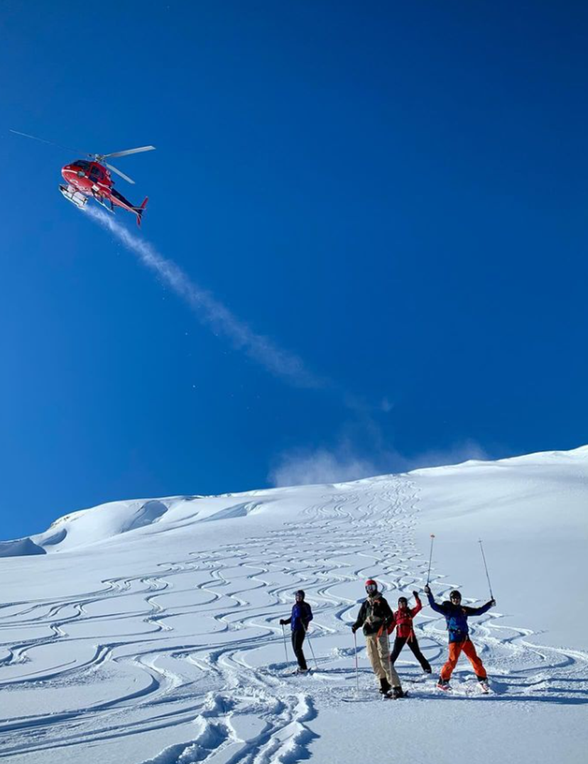 group of four heli skiers at the bottom of their tracks with heli flying by