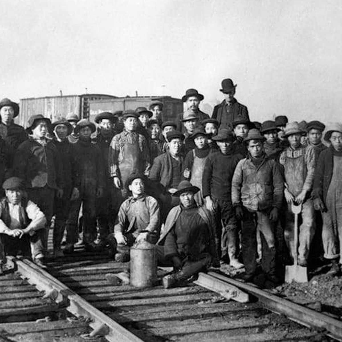A group of railroad workers standing on train tracks, with boxcars visible in the background.