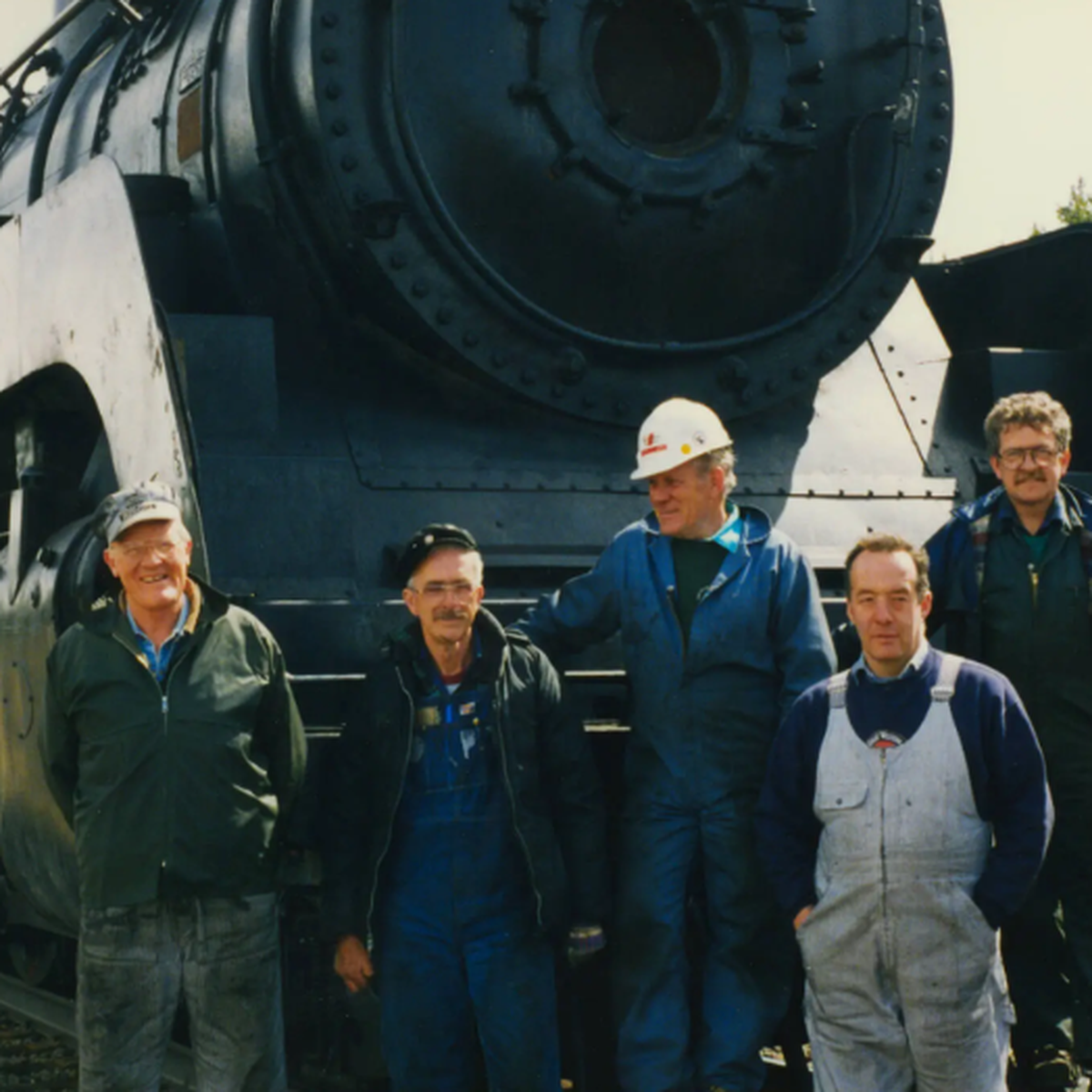 Five men in work clothes stand in front of a large black steam locomotive