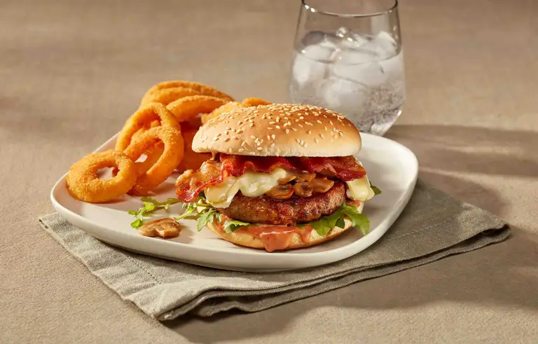 Burger de porc assaisonné garni de bacon, fromage, champignons, laitue et sauce avec rondelles d'oignons