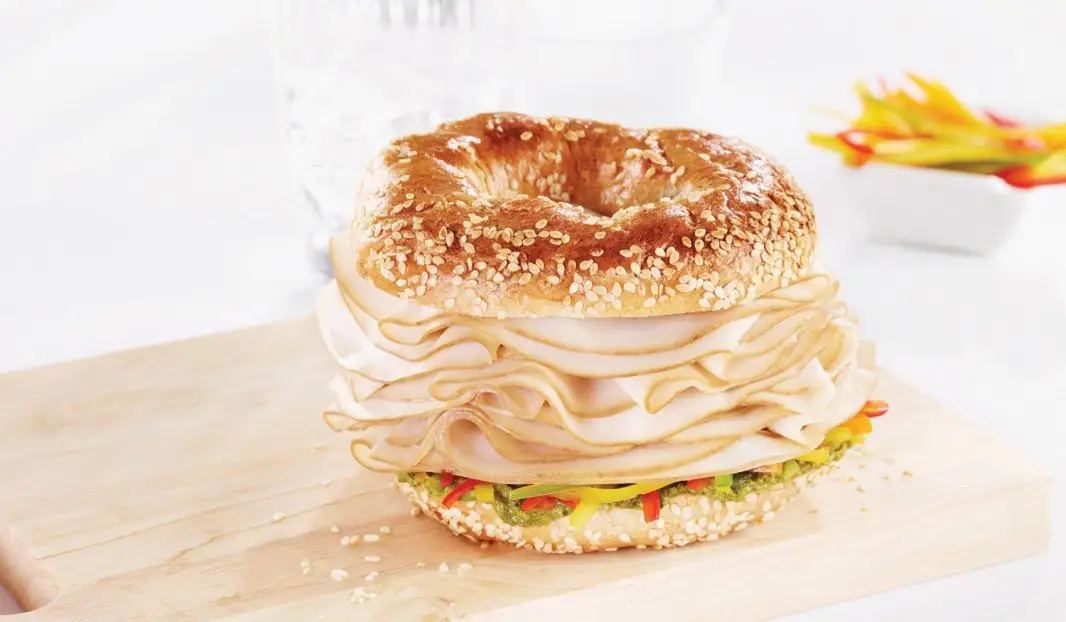 Bagel au sésame garni de poulet fumé, poivrons et pesto