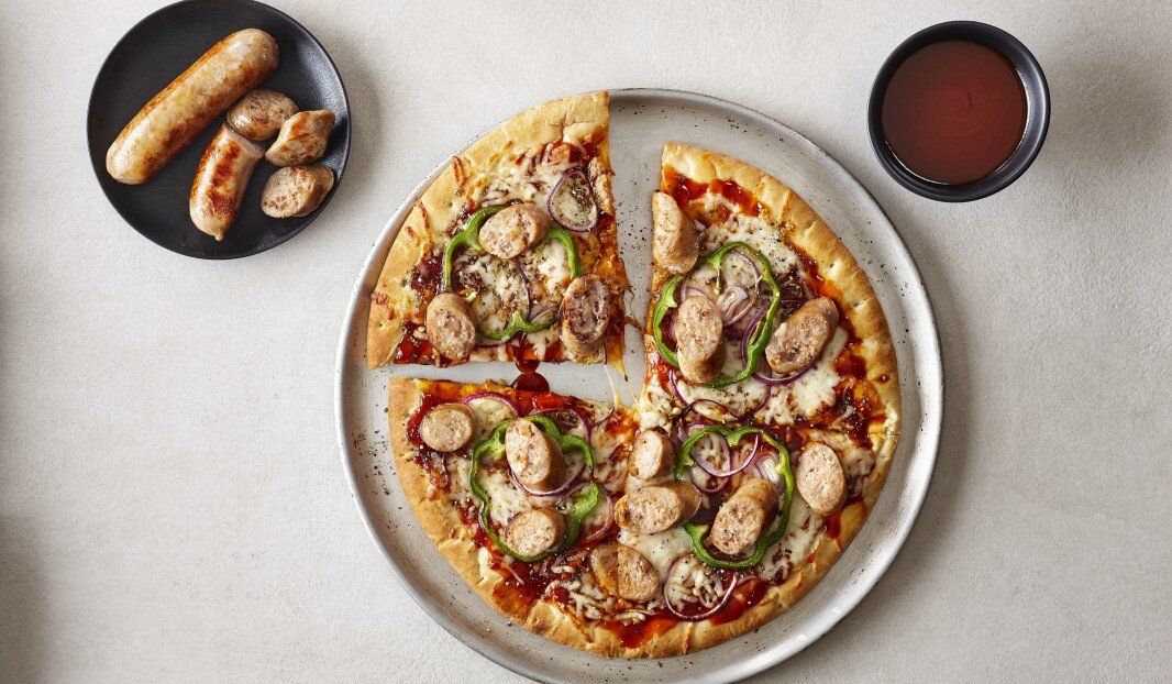 Pizza avec saucisses, poivrons et oignons, accompagnée de saucisses et sauce.