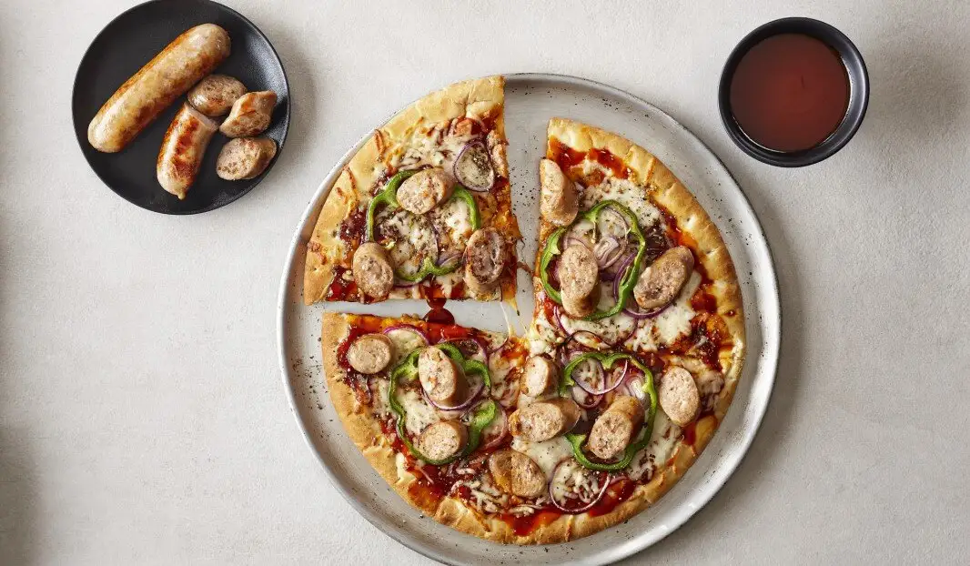 Pizza avec saucisses, poivrons et oignons, accompagnée de saucisses et sauce.