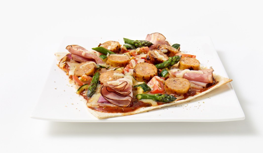 Pizza garnie de saucisse italienne, jambon fumé et légumes grillés