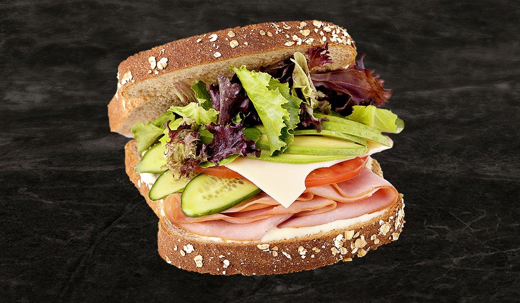 Sandwich au pain complet avec jambon, fromage, tomates, concombres et légumes verts.