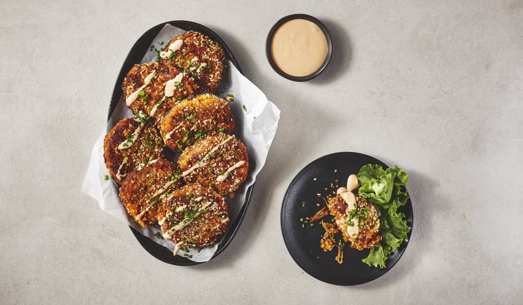 Beignets de porc croustillants sur une assiette noire avec sauce de trempage, garnis d'herbes et servis avec de la laitue sur le côté.