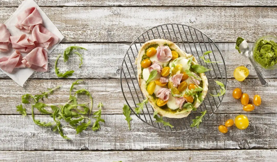 Pizza sur pain naan avec pesto, mozzarella, jambon et roquette