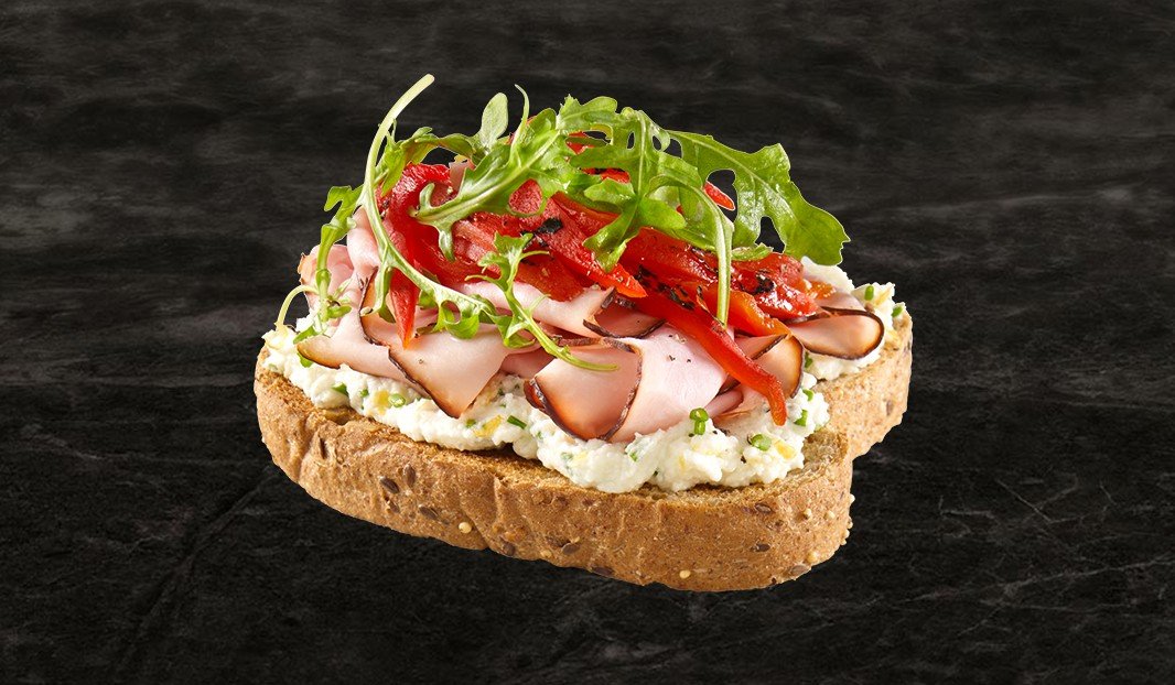 Tartine au jambon, poivrons rôtis, roquette et tartinade sur pain grainé.