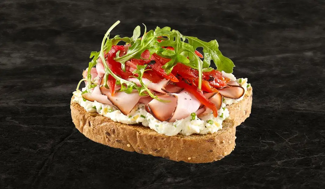 Tartine au jambon, poivrons rôtis, roquette et tartinade sur pain grainé.