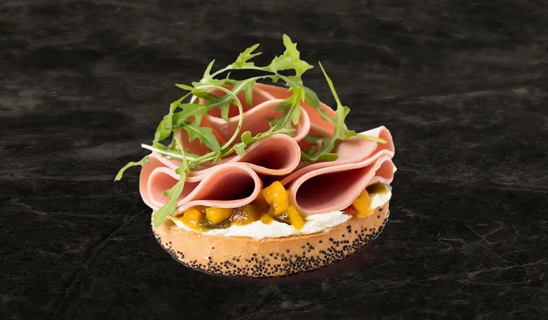 Tartine sur bagel au fromage, mangue, simili poulet et roquette.
