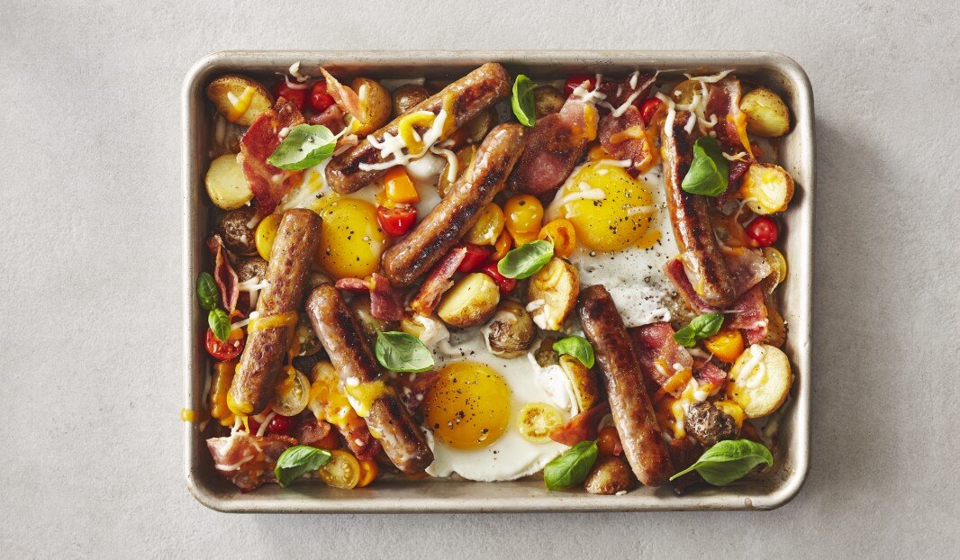 Plat de petit-déjeuner avec saucisses, œufs, bacon, pommes de terre, tomates et basilic.