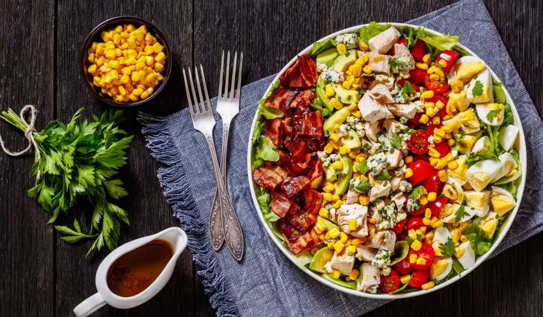 Salade avec laitue, tomates cerises, maïs, œufs, poulet grillé, bacon et herbes.