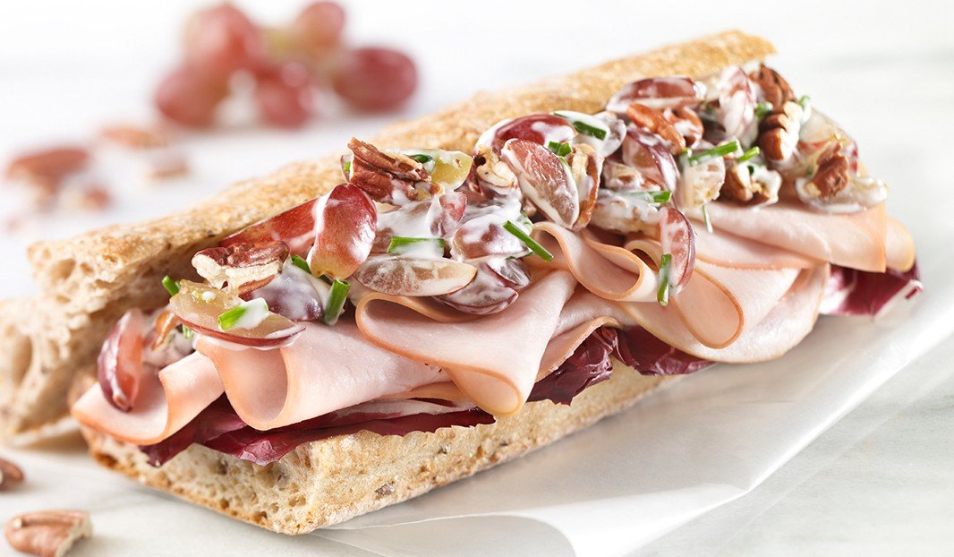 Baguette garnie de poulet, raisins, noix, verdures et sauce crémeuse.