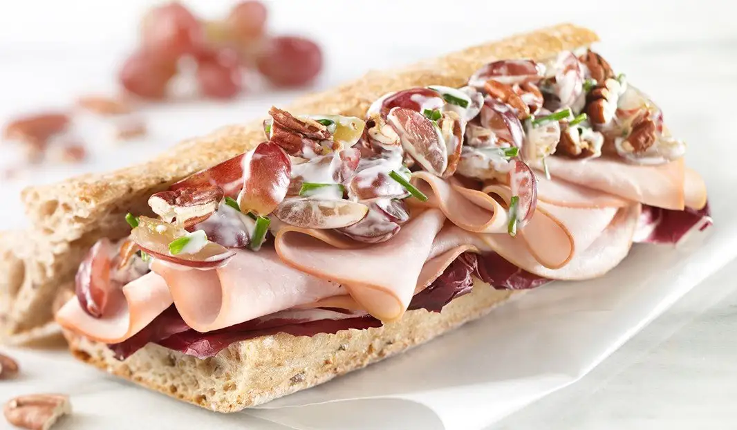 Baguette garnie de poulet, raisins, noix, verdures et sauce crémeuse.