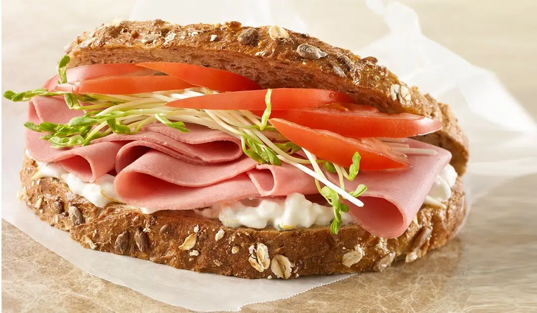 Sandwich au pain grainé, bologne, tomates, germes et tartinade crémeuse.