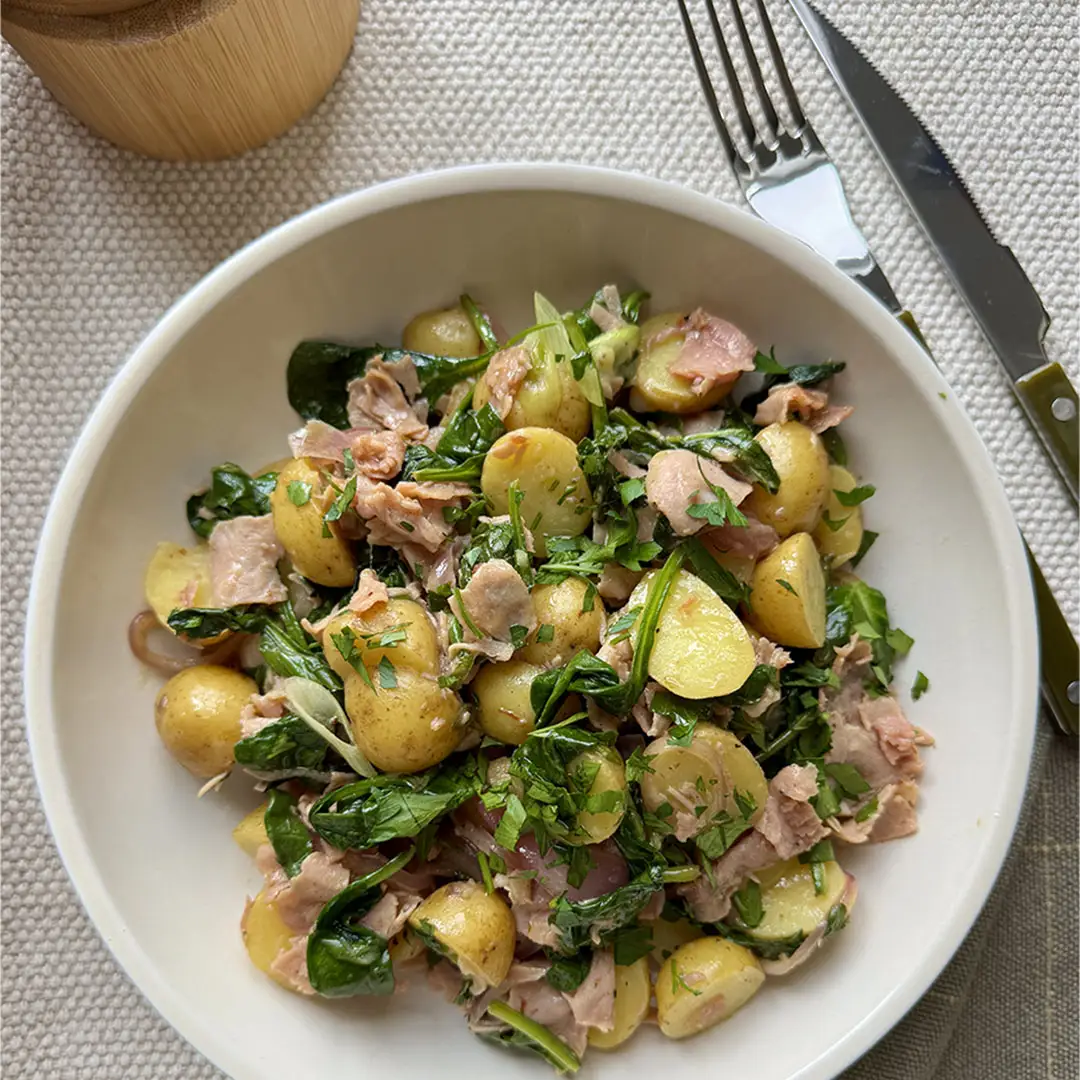 Salade de pommes de terre au jambon blanc cuit Smart & Natural avec épinards servie dans une assiette blanche avec des ustensiles