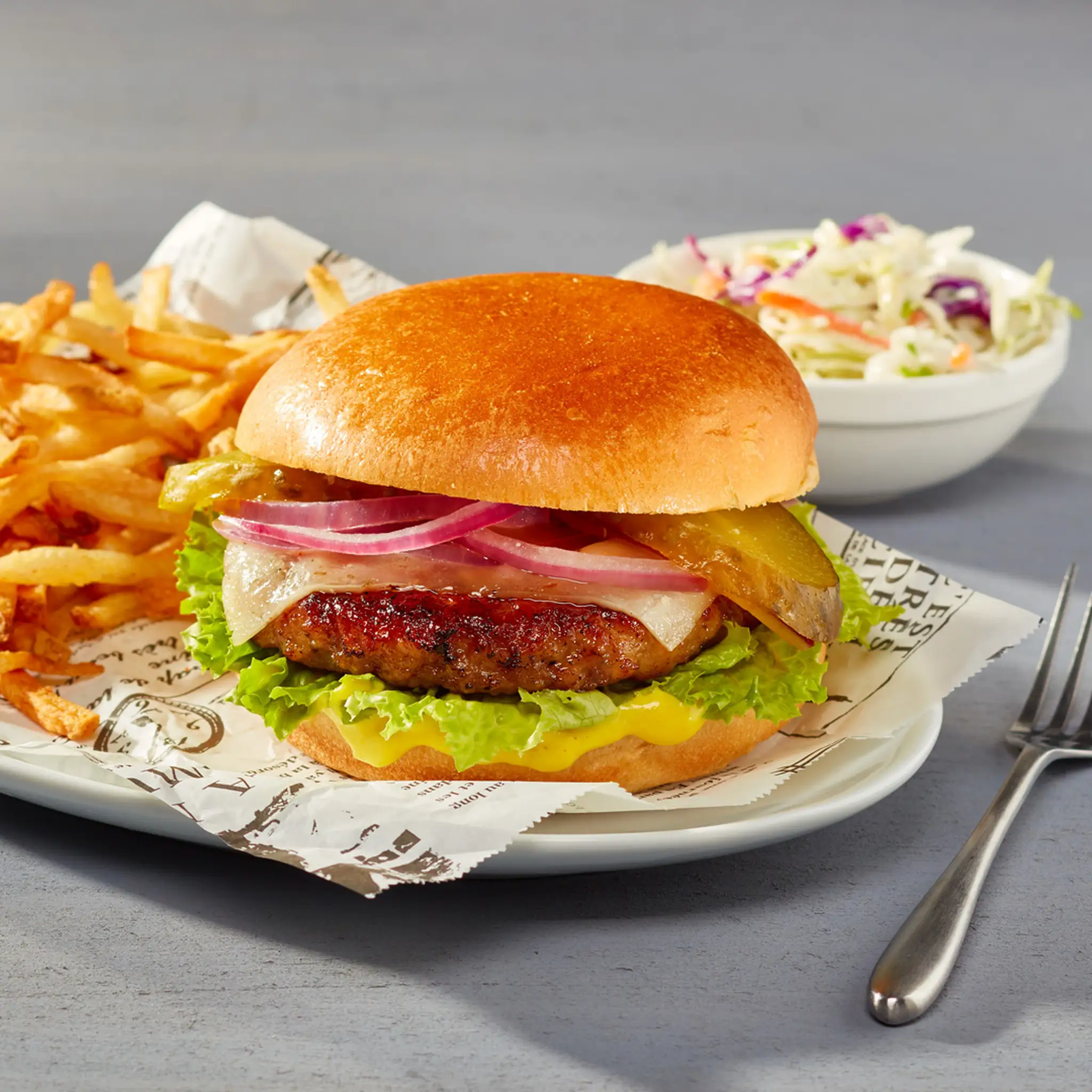 Burger de porc assaisonné garni de laitue, fromage, oignons rouges, cornichons avec frites et salade de choux