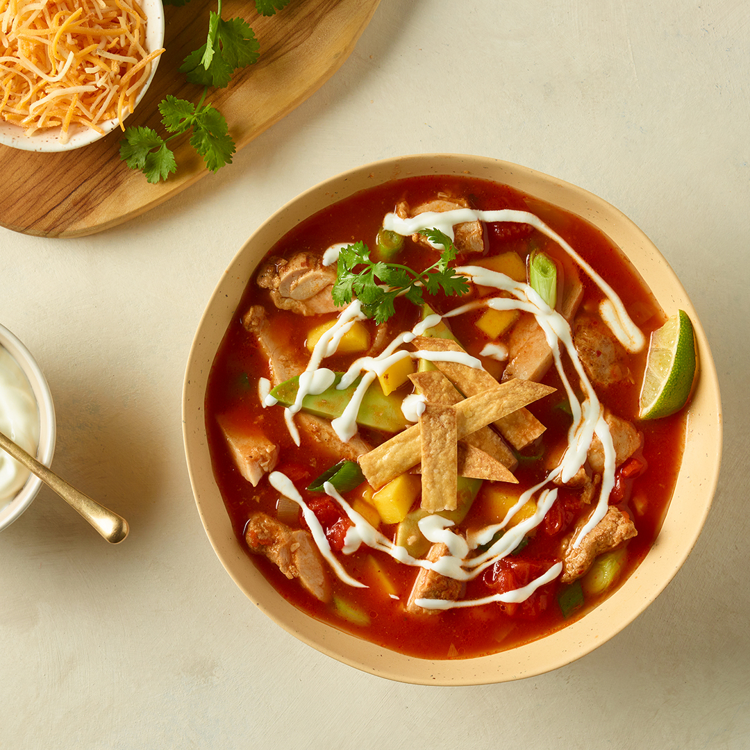 Soupe au poulet à la mexicaine avec tortillas grillés, quartier de lime et un filet de crème sure dans un bol sur un comptoir de cuisine