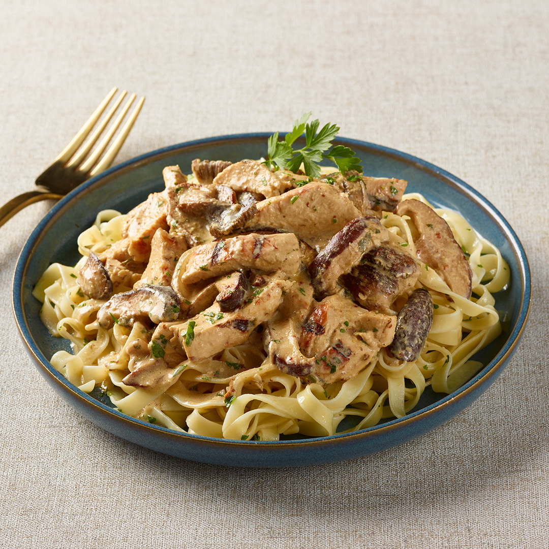 Lanières de poitrine de poulet à la crème de champignons et moutarde servies sur des pâtes longues dans une assiette bleue avec une fourchette or