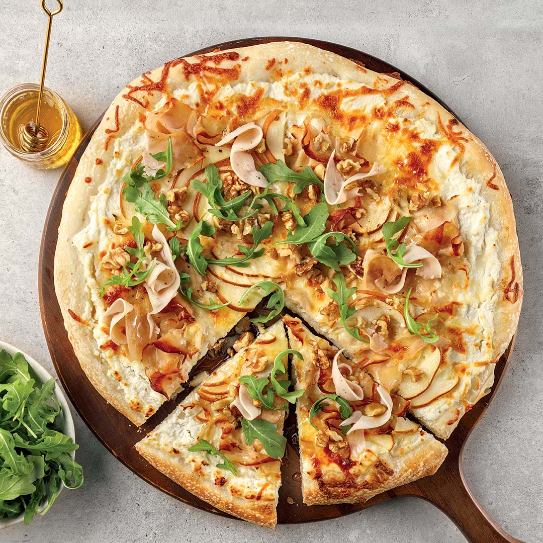 Pizza dinde et poire sur une planche en bois avec de la roquette et du miel