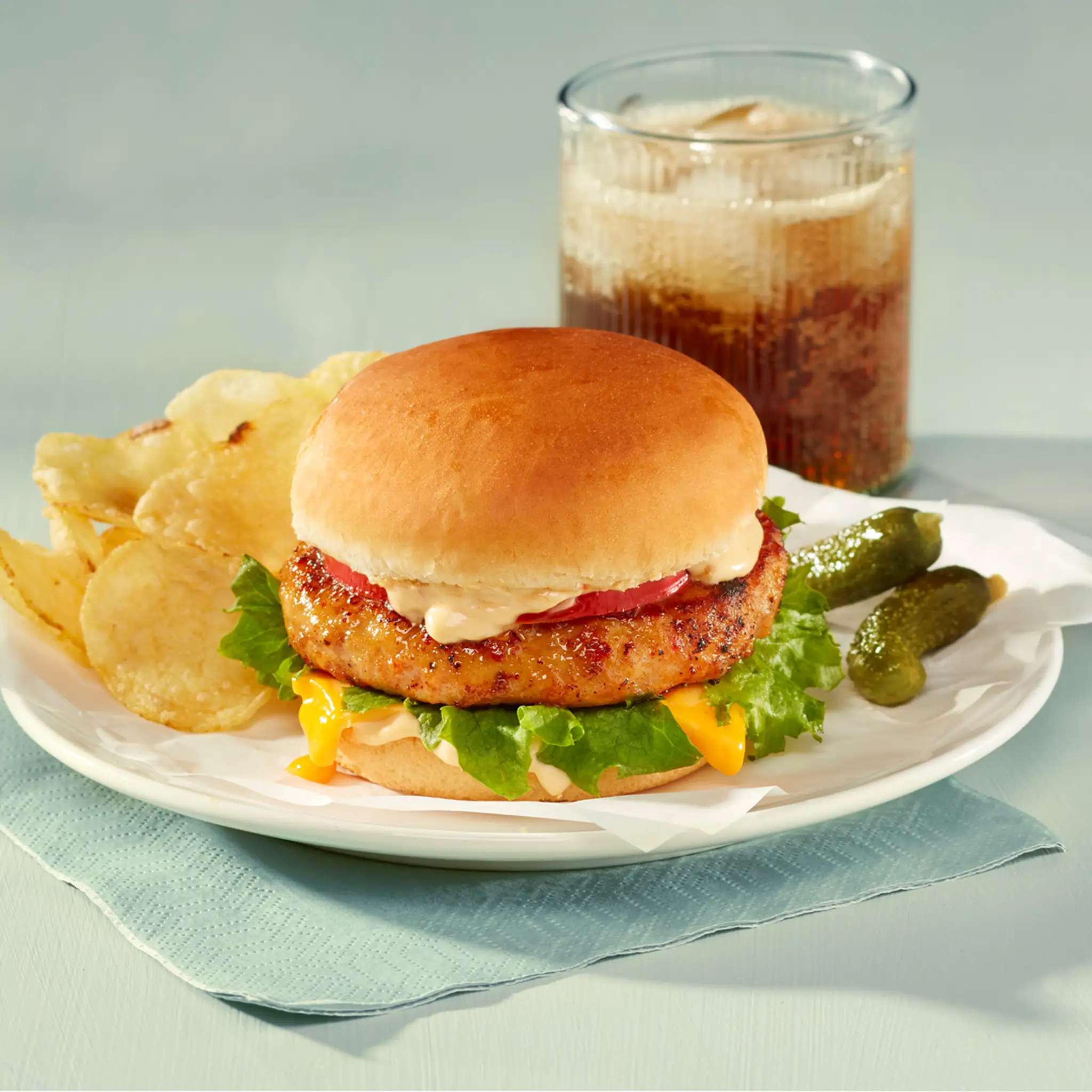 Burger de poulet assaisonné garni de laitue, tomate, mayo avec un à-côtés de chips et boisson gazeuse