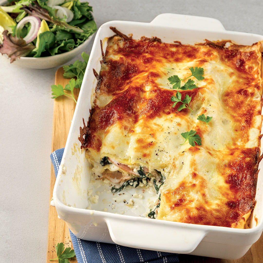 Lasagne au jambon, épinards et ricotta dans un plat blanc accompagnée d'une salade