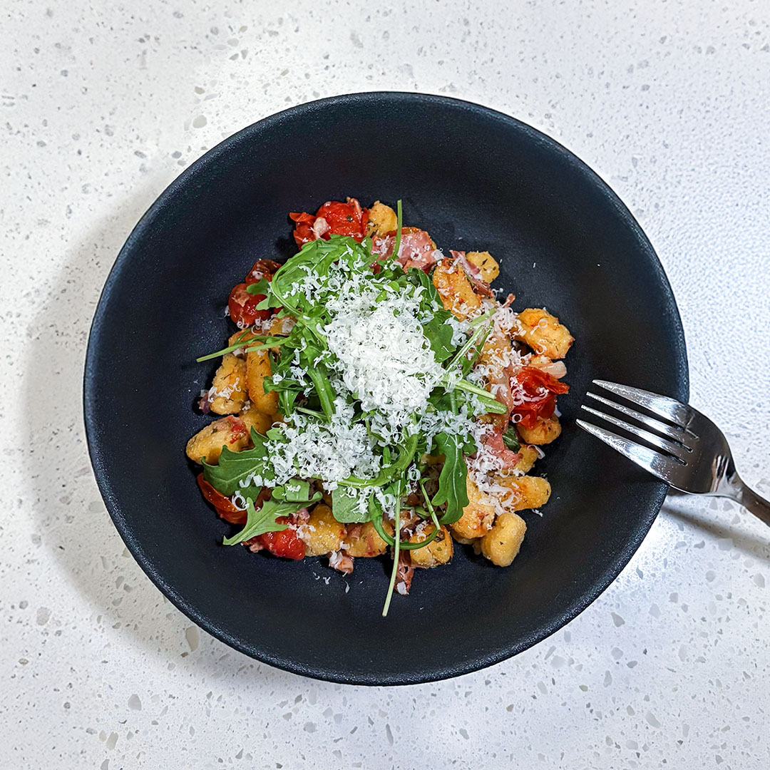 Gnocchis rôtis au jambon fumé forêt noire Smart & Natural avec de la roquette et du parmesan dans un bol noir