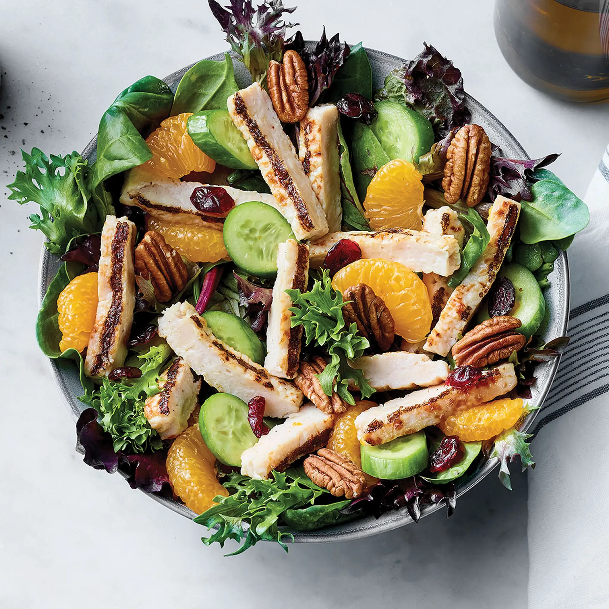 Salade de poulet avec lanières assaisonnées, mélanges printaniers, concombre, pacanes, canneberges séchées et clémentine