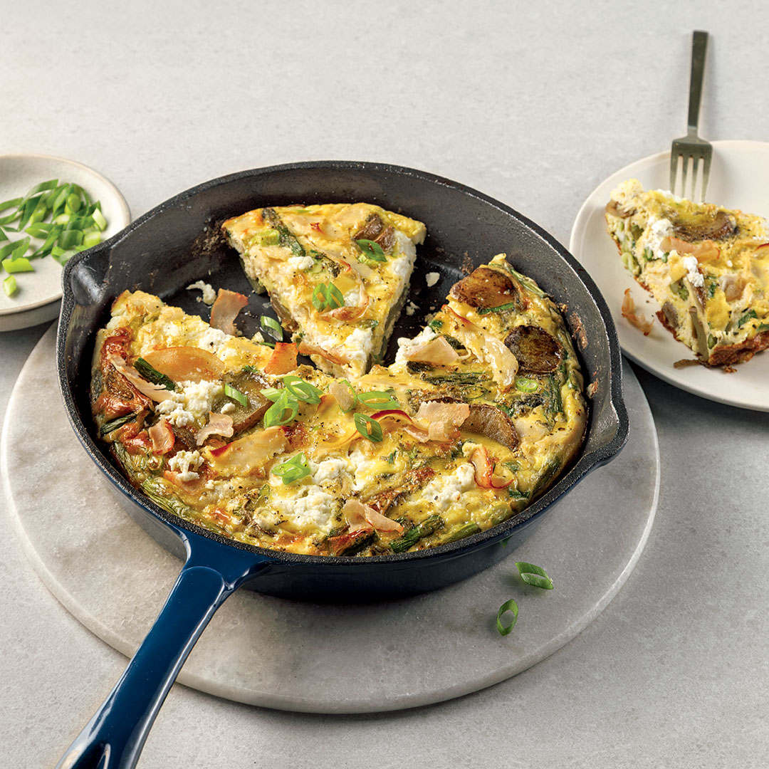 Frittata à la dinde, pommes de terre et fromage de chèvre dans une poêle sur un comptoir gris avec un portion servie dans une assiette sur le côté