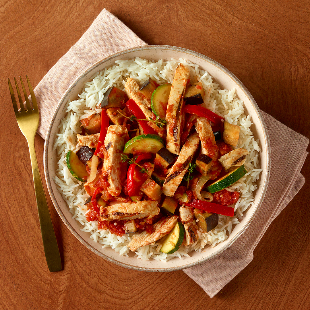 Lanières de poulet à la basquaise avec aubergine et courgette servies dans une assiette rose avec une serviette rose et une fourchette or