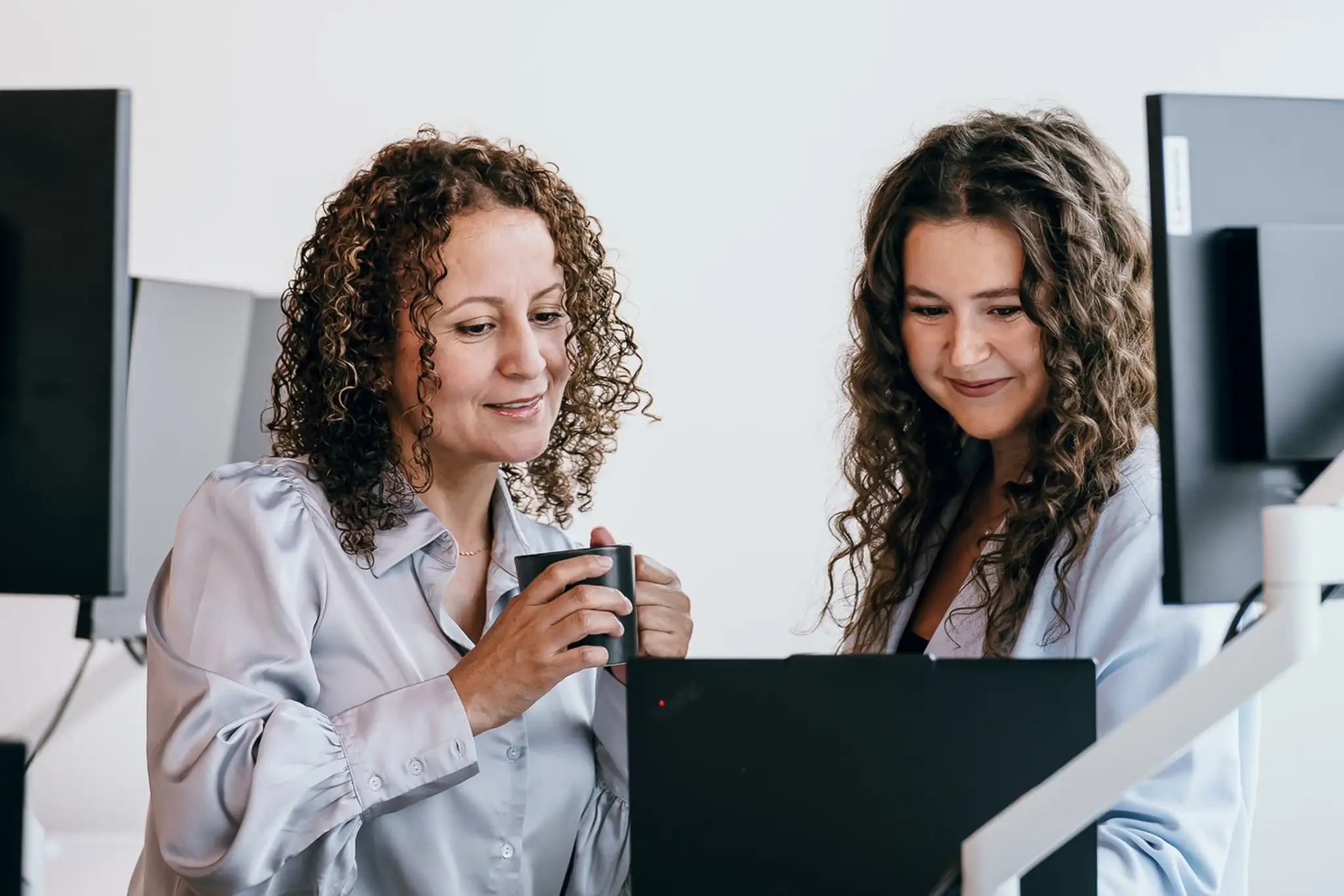 Deux personnes se retrouvent derrière trois écrans en train de discuter.