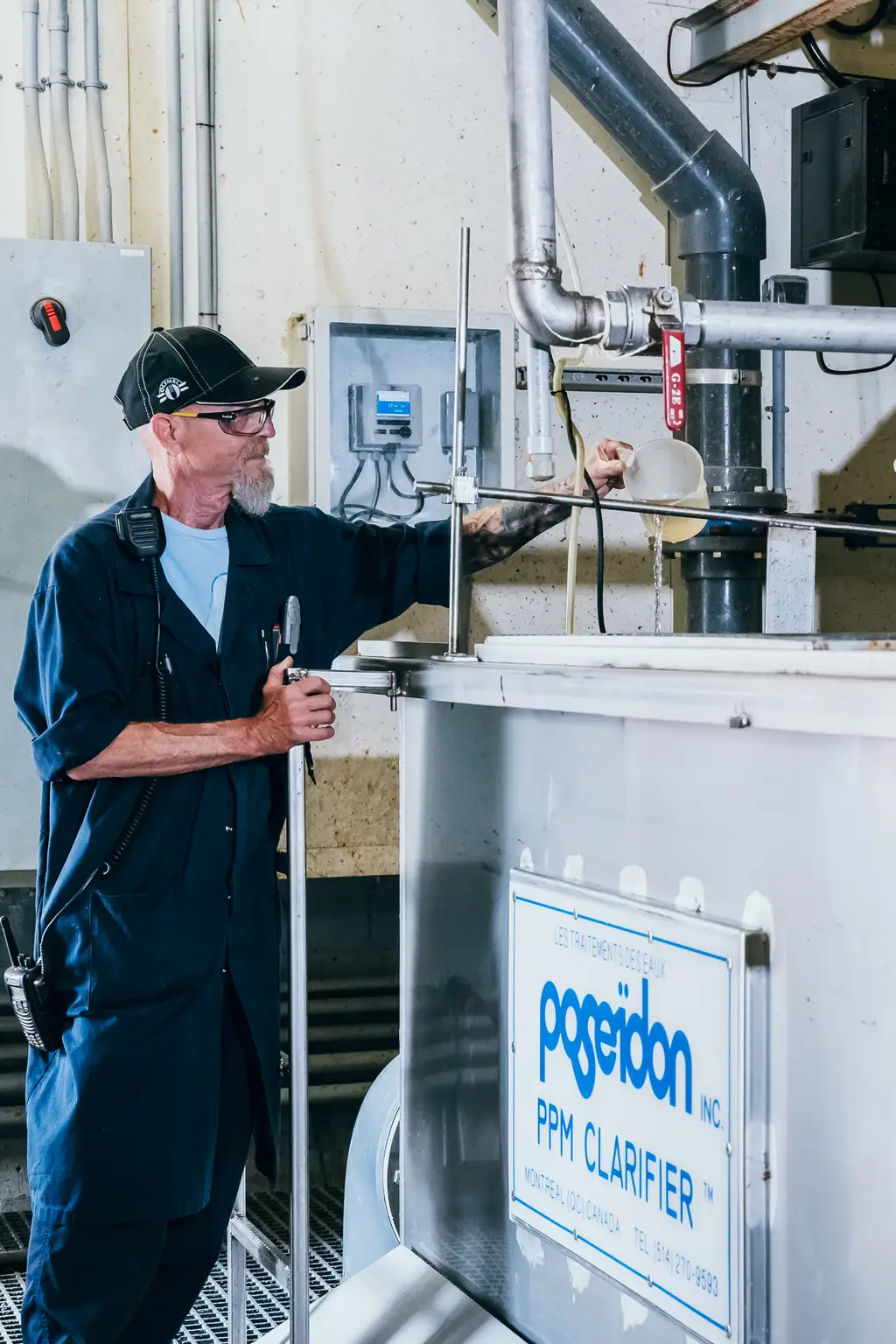 Homme en uniforme sombre et casquette opérant un équipement industriel portant l’inscription "PPM Clarifier" dans une installation, tenant une clé et ajustant les commandes.