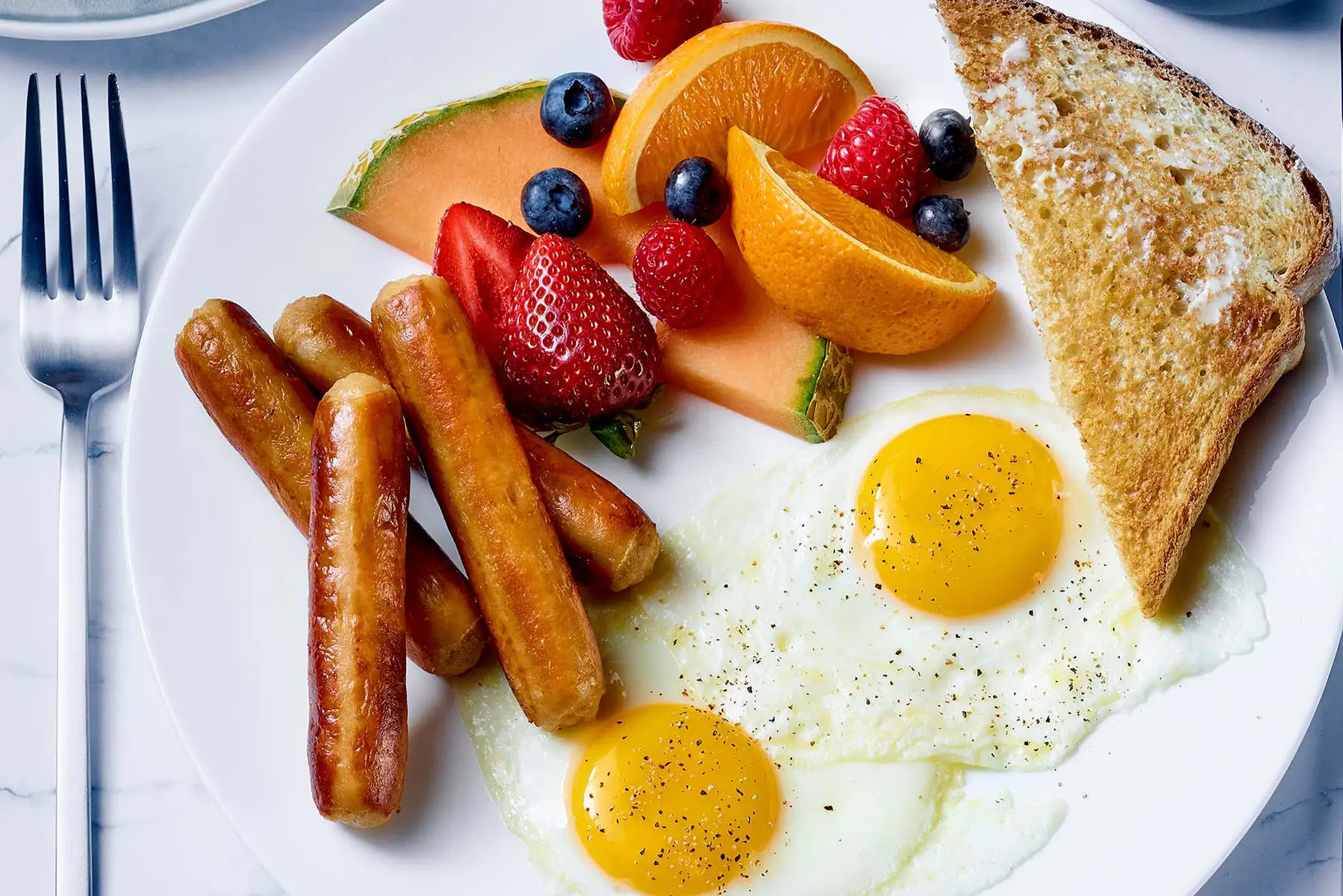 Repas déjeuner avec saucisses, oeufs, toast et fruits