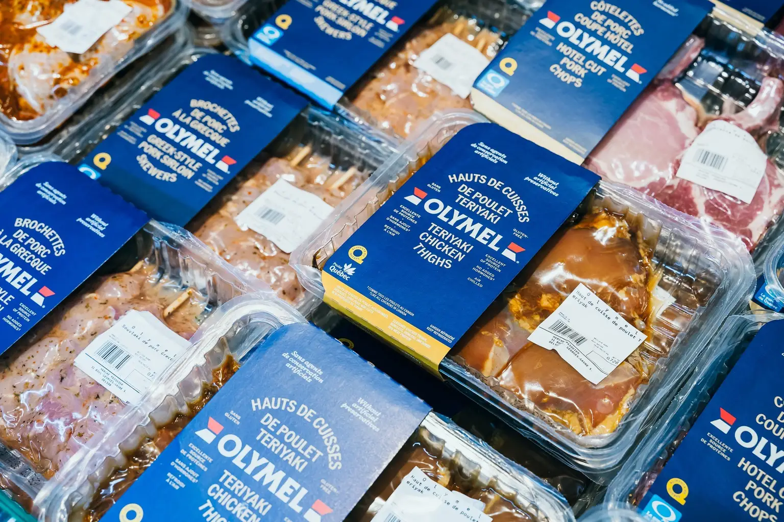 Produits de poulet marinés emballés avec des étiquettes bleues, portant la marque "OLYMEL", exposés dans un magasin.