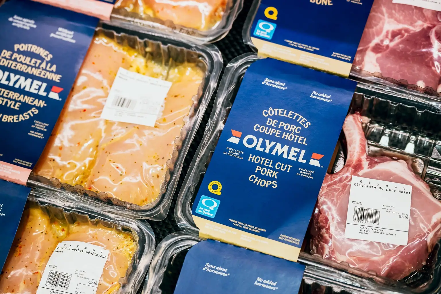 Viandes crues emballées, incluant du poulet mariné et des côtelettes de porc, étiquetées avec la marque “Olymel” dans un présentoir d’épicerie.
