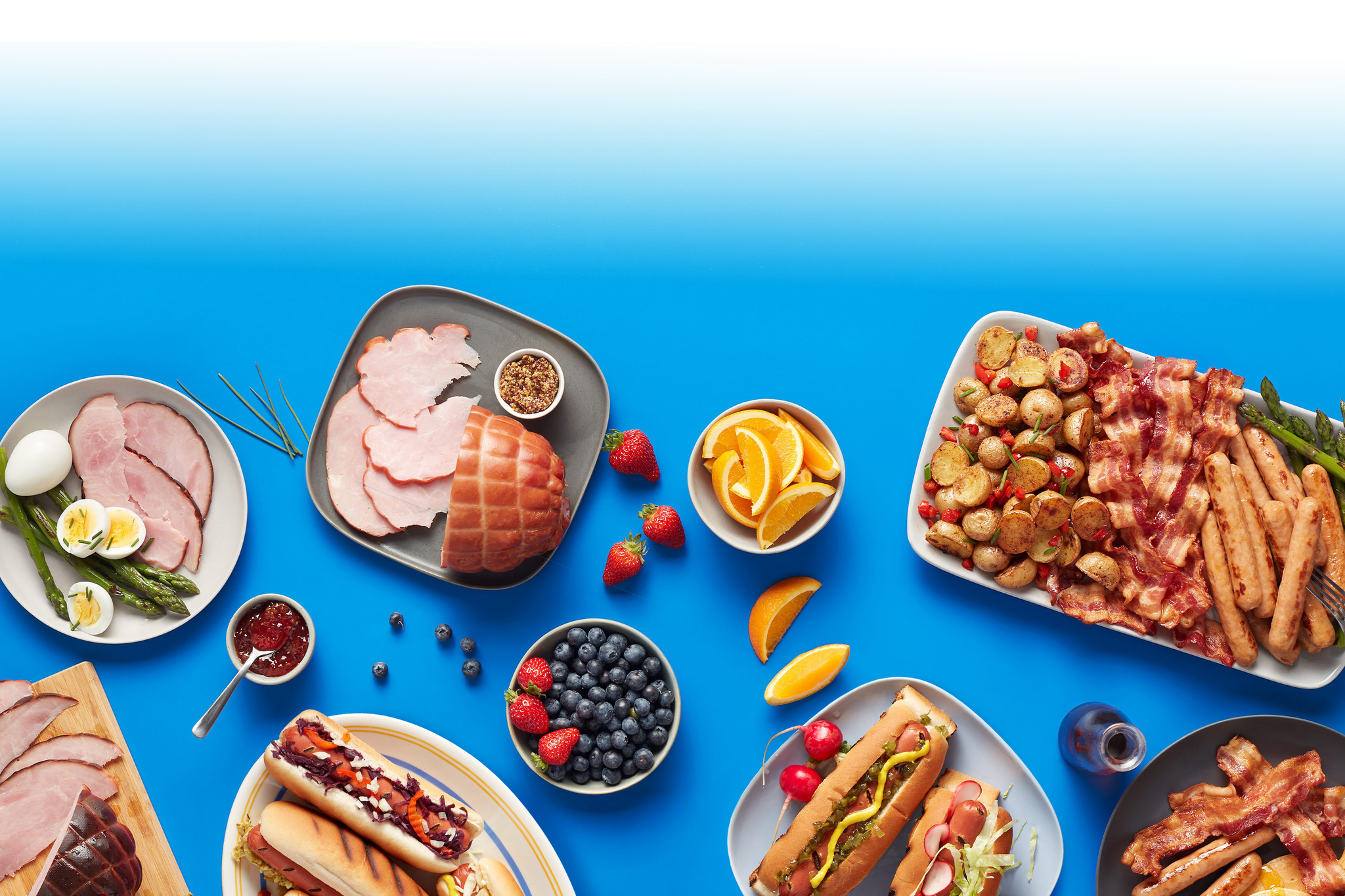 Tablée avec différents plats de saucisses, bacons, jambons, hotdog, patates et fruits